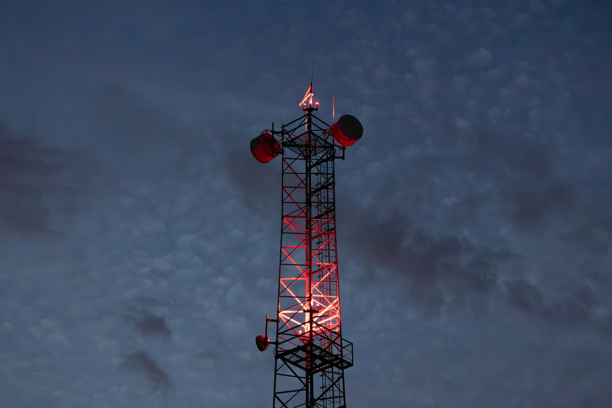 A lattice communication tower with red beacons against the evening sky